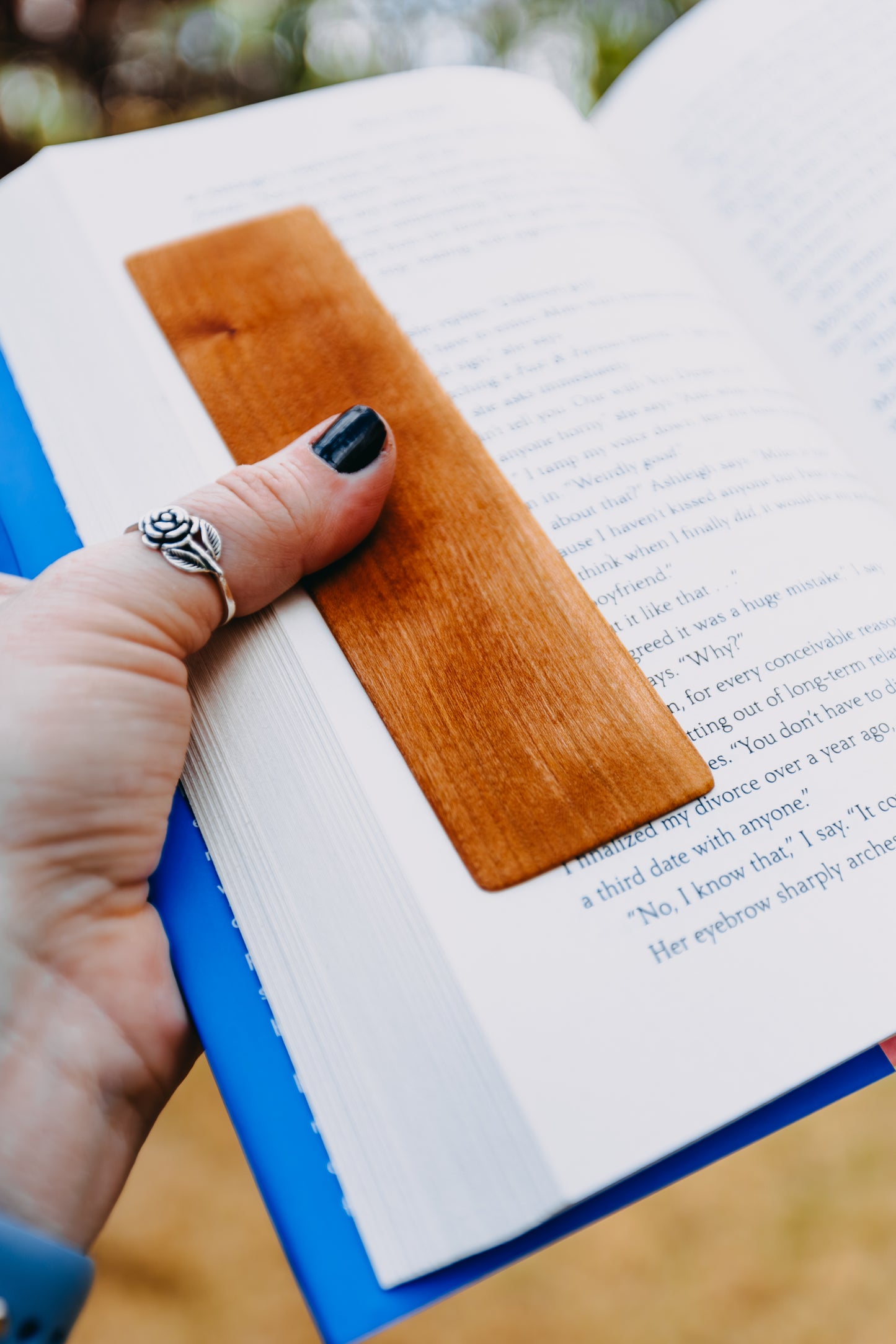 Hand with a wooden cherry edge grain bookmark on an open book