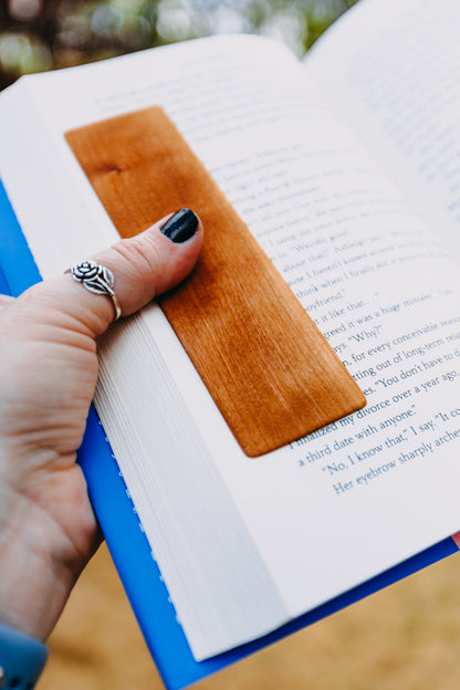 Hand with a wooden cherry edge grain bookmark on an open book