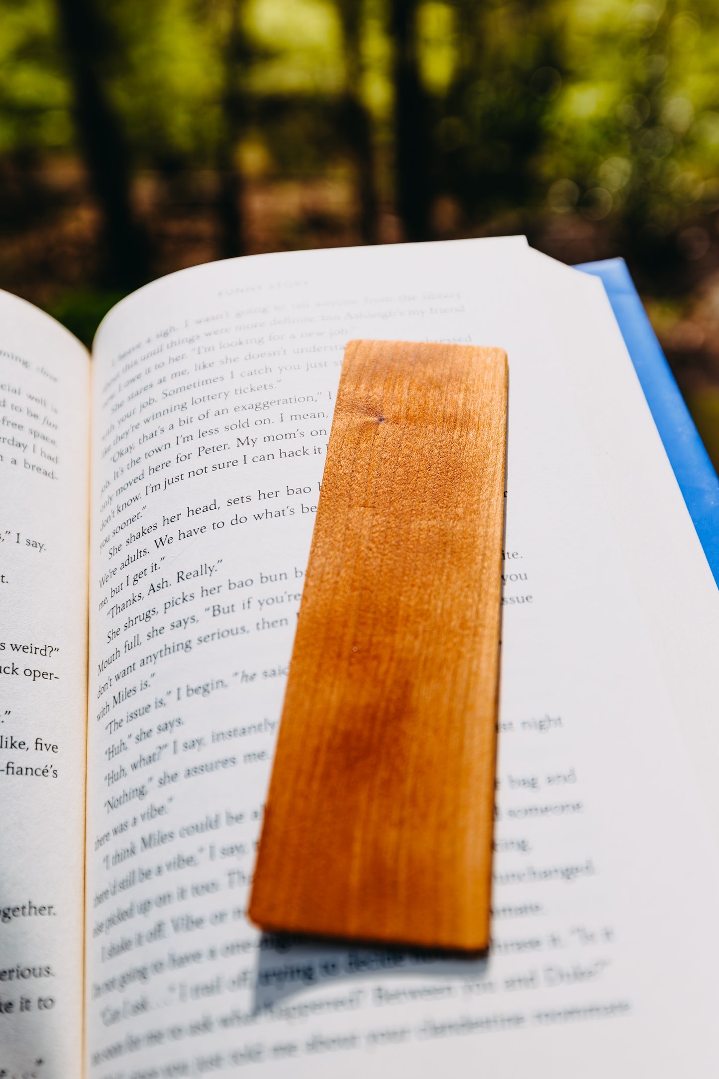 Open book with a wooden cherry edge grain bookmark in a forest setting