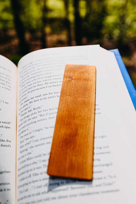 Open book with a wooden cherry edge grain bookmark in a forest setting