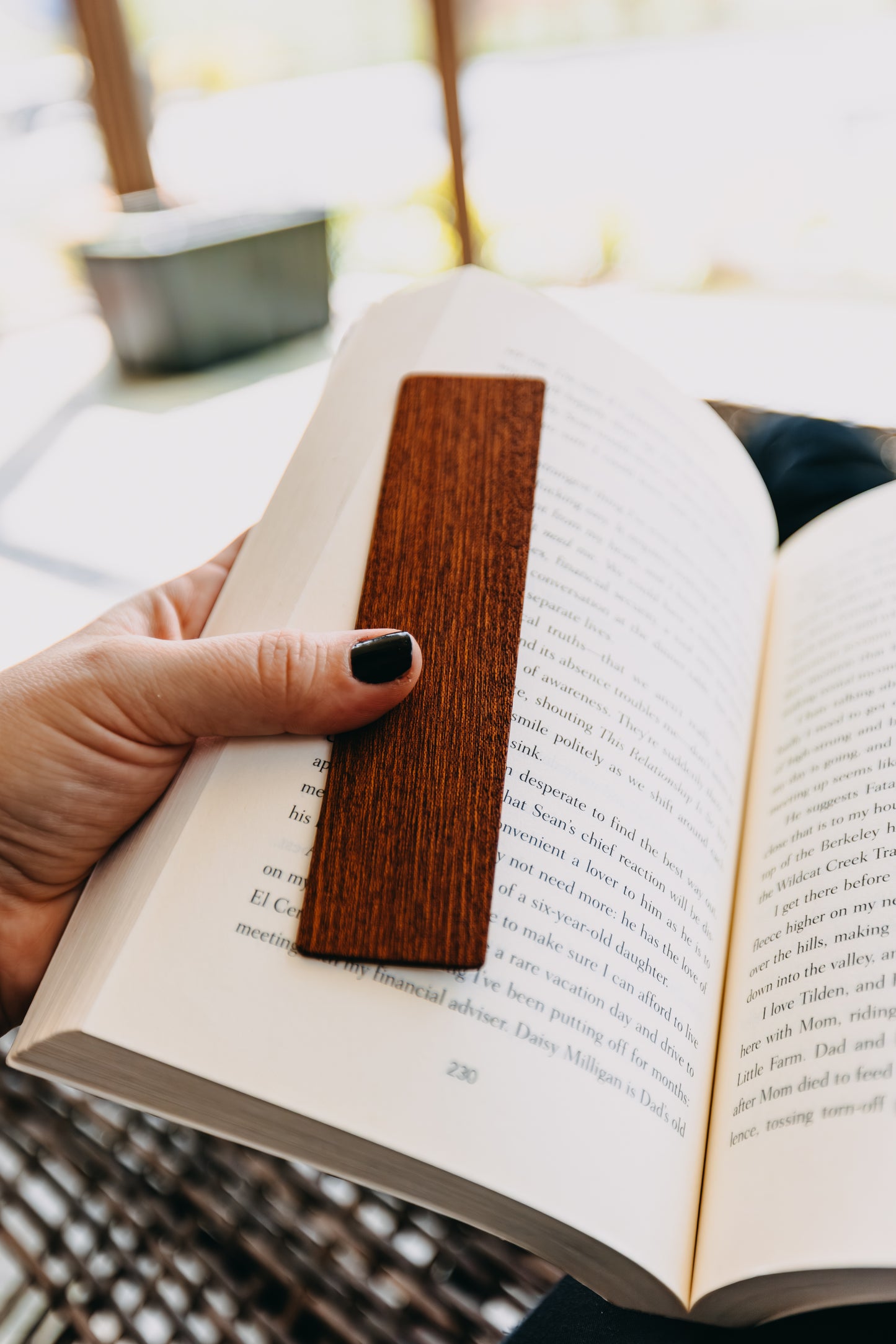 Hand holding an open book with a wooden sapele edge grain bookmark on a blurred background