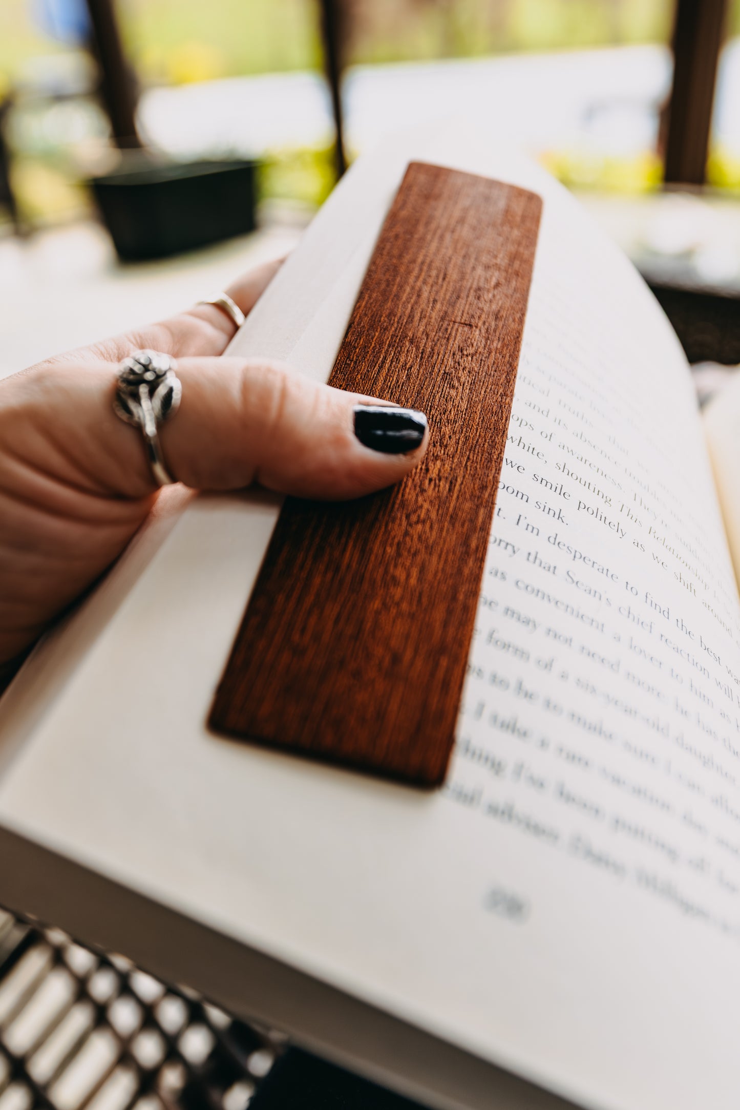 Hand holding an open book with a wooden sapele edge grain  bookmark.