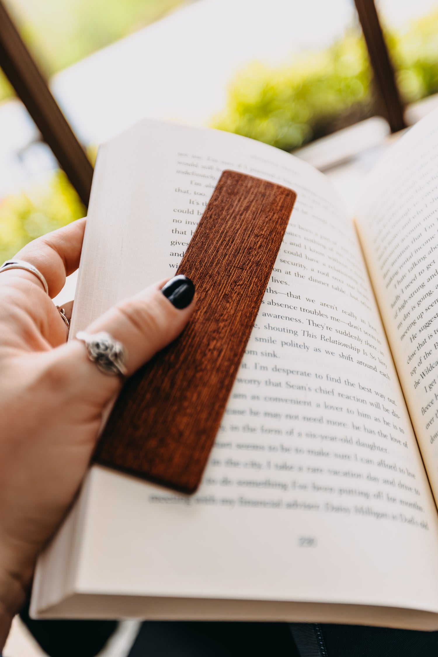 Person holding an open book with a wooden sapele edge grain bookmark.