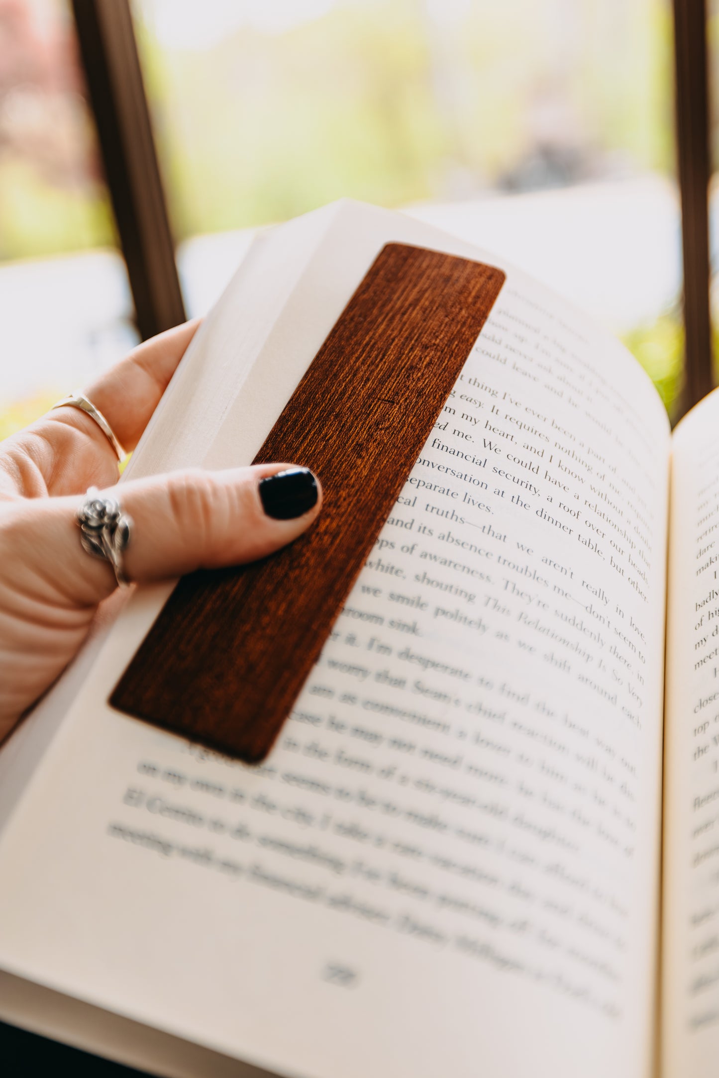 Hand holding an open book with a wooden sapele edge grain bookmark, blurred background