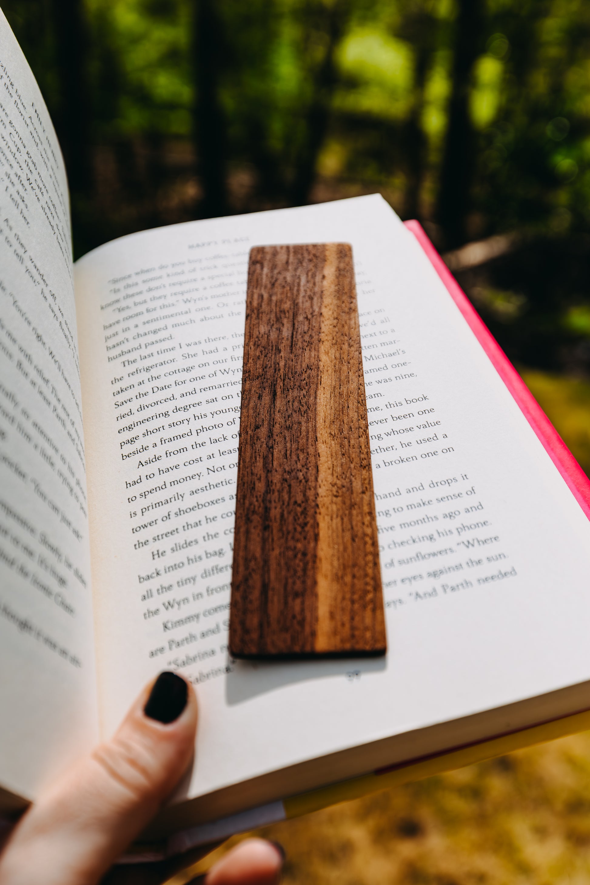 Wooden black walnut edge grain bookmark on an open book with a blurred natural background
