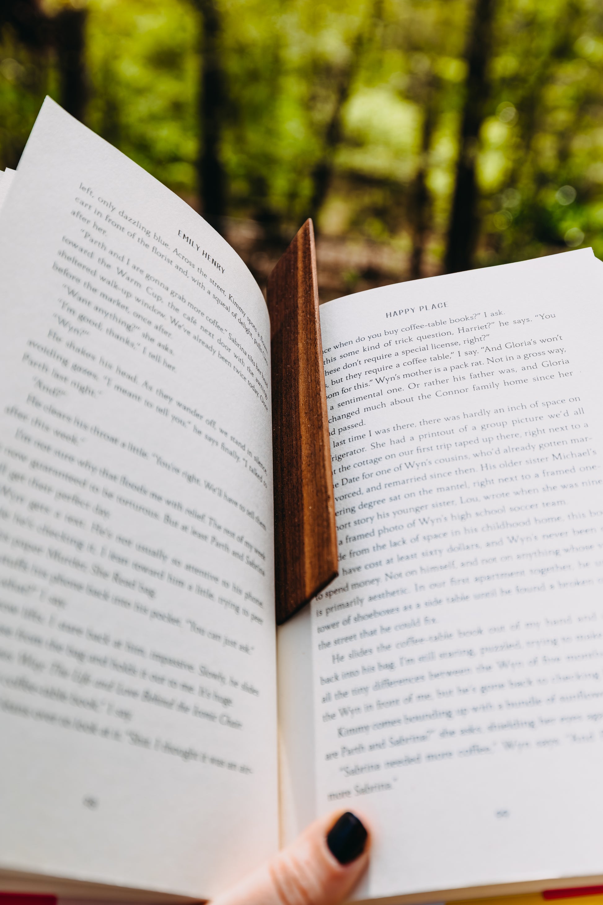 Open book and a wooden black walnut edge grain bookmark held against a blurred natural background