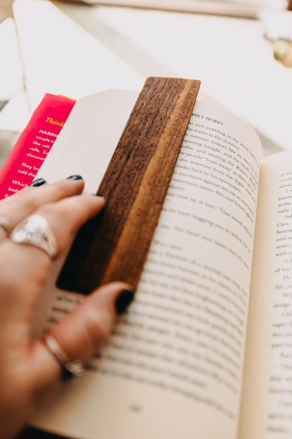 Hand holding a wooden black walnut edge grain bookmark in an open book