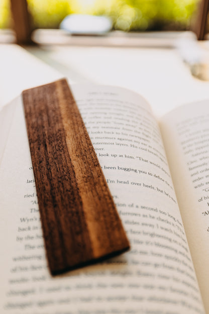 Wooden black walnut edge grain bookmark on an open book with a blurred natural background